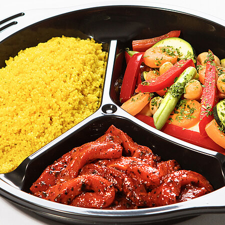Ein Mikrowellenmenü in einer Plastikschale mit drei getrennten Fächern. In einem Fach ist Schweinegeschnetzeltes, in einem Gemüse und in einem gekochter Couscous.