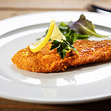 Ein Schnitzel auf einem weißen Teller, garniert mit Zitrone, einem Salatblatt und einem Kraut. 
