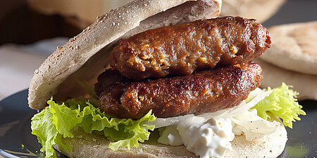 Ein belegtes Brötchen mit Salat, Remoulade und gebratenem Hackfleisch in länglicher Form-