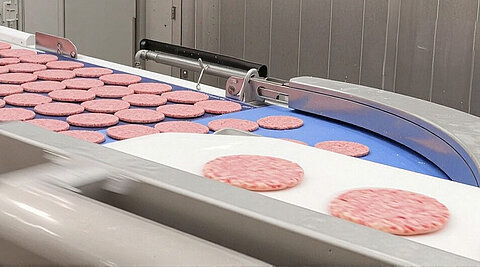 Ein Fließband mit vielen flachen Burger Patties, die eingefroren werden. 