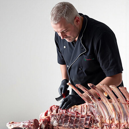 Ein Mann in einem dunkelblauen Arbeitskittel schneidet Steaks aus einem großen Rippenstück.
