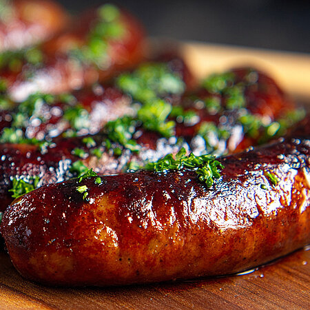 Gegrillte Würstchen liegen nebeneinander. Sie sind aus dunklem Fleisch und kross gegrillt. Sie sind mit Kräutern bestreut. 