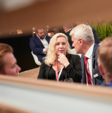 Eine Frau und ein Mann sprechen während der Anuga Messe miteinander. Sie tragen Business-Kleidung. Um sie herum sind weitere Besucher der Messe.