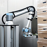 Ein Roboter wickelt Folie um einige Verpackungskartons, um diese miteinander zu verbinden.