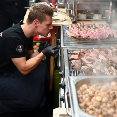 Ein Mitarbeiter von Westfleisch grillt und brät auf der Anuga verschiedene Fleischsorten und Pilze.